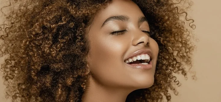 Close-up of a woman's face. She is smiling and looking upwards away from the camera.